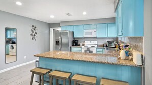 A kitchen with blue cabinets, a granite countertop, and a stainless steel refrigerator.