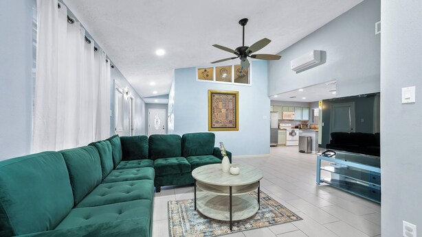 A modern living room with a green sectional sofa, a round coffee table, and a ceiling fan.