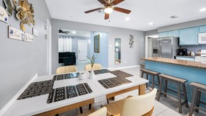A modern kitchen with blue cabinets, a stainless steel refrigerator, and a dining area with a white table and patterned placemats.