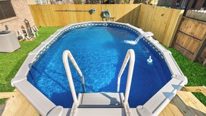 An above-ground swimming pool with a wooden deck, metal ladder, and a hose for filling.