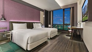 Une chambre d’hôtel avec deux lits, un bureau, une chaise, une télévision et une grande fenêtre donnant sur la ville.