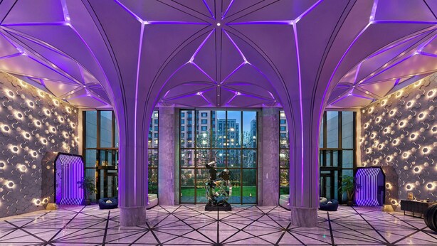 Un hall d’entrée moderne avec un plafond au design géométrique, de grandes fenêtres et un mur orné de motifs.