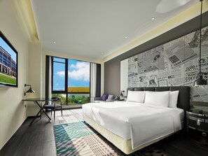 Een moderne hotelkamer met een groot bed, uitzicht op de omgeving, een bureau met stoel, en een muur met krantenknipsels.