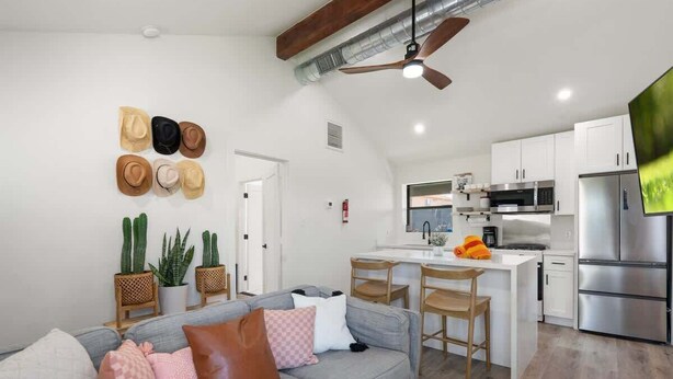 A modern kitchen with stainless steel appliances, a dining area with wooden chairs, and a grey sofa with multiple cushions. - Shared fun Pickleball, Theater & Pool | DT Phoenix (Phoenix)