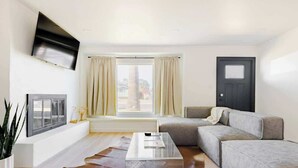 A modern living room with a grey sofa, a glass coffee table, a mounted TV, and a window with curtains. - Renovated Retreat, Old Town Scottsdale, Sleeps 6 (Scottsdale)