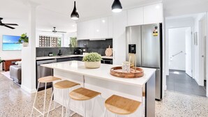 Una cocina moderna con armarios blancos, un refrigerador de acero inoxidable y una isla central con taburetes de bar.