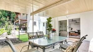Un patio al aire libre con una mesa y sillas de vidrio, rodeado por un muro blanco y un área cubierta.