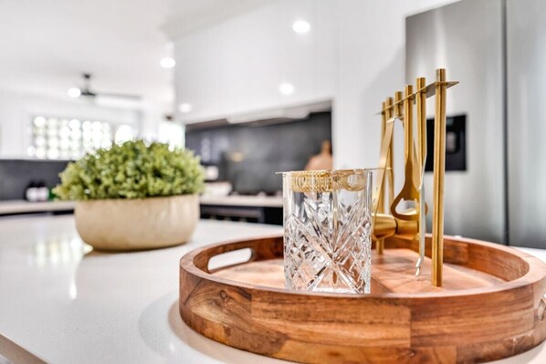 A modern kitchen with a wooden tray holding a glass and gold utensils.