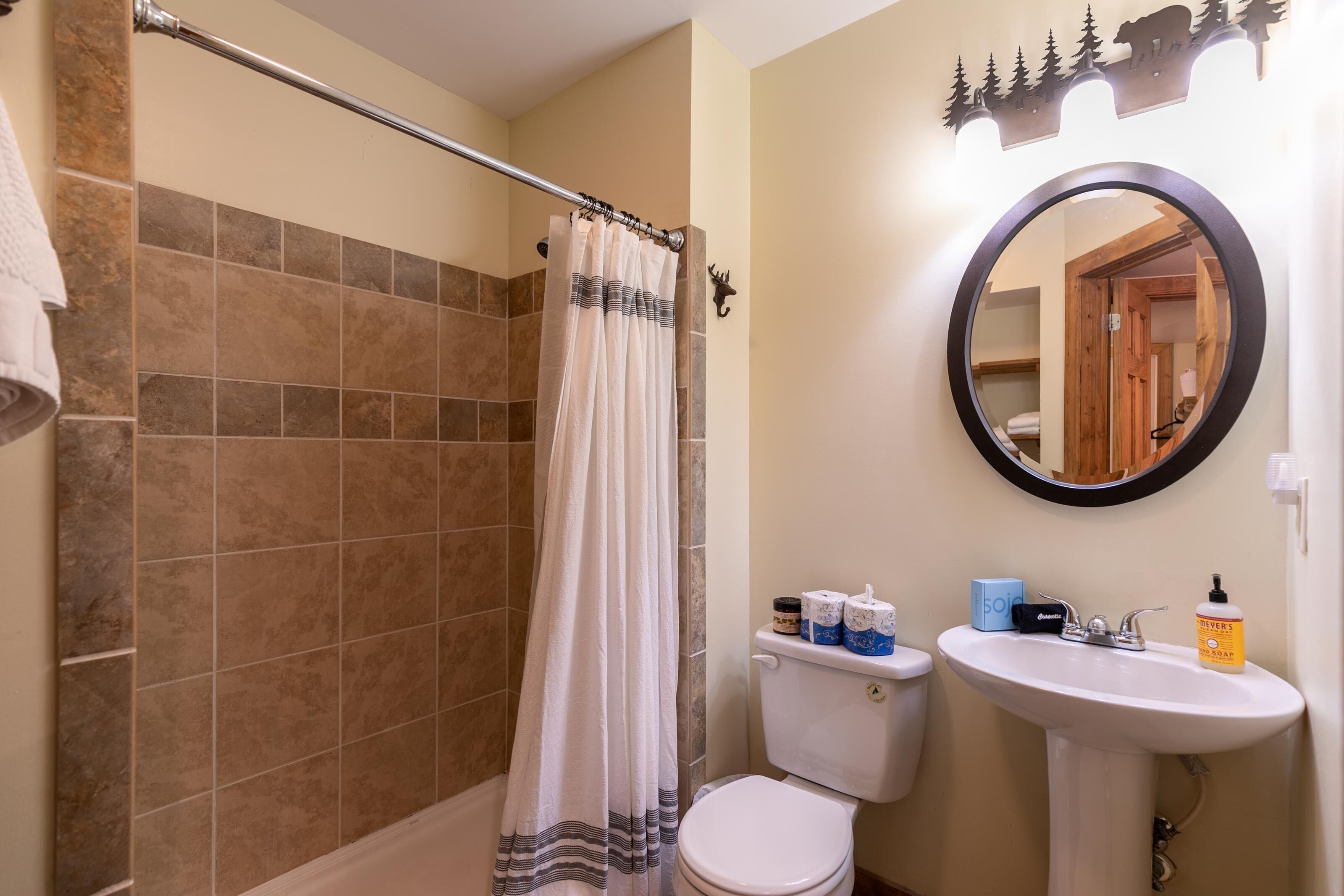 A bathroom with a shower, toilet, sink, and a mirror.