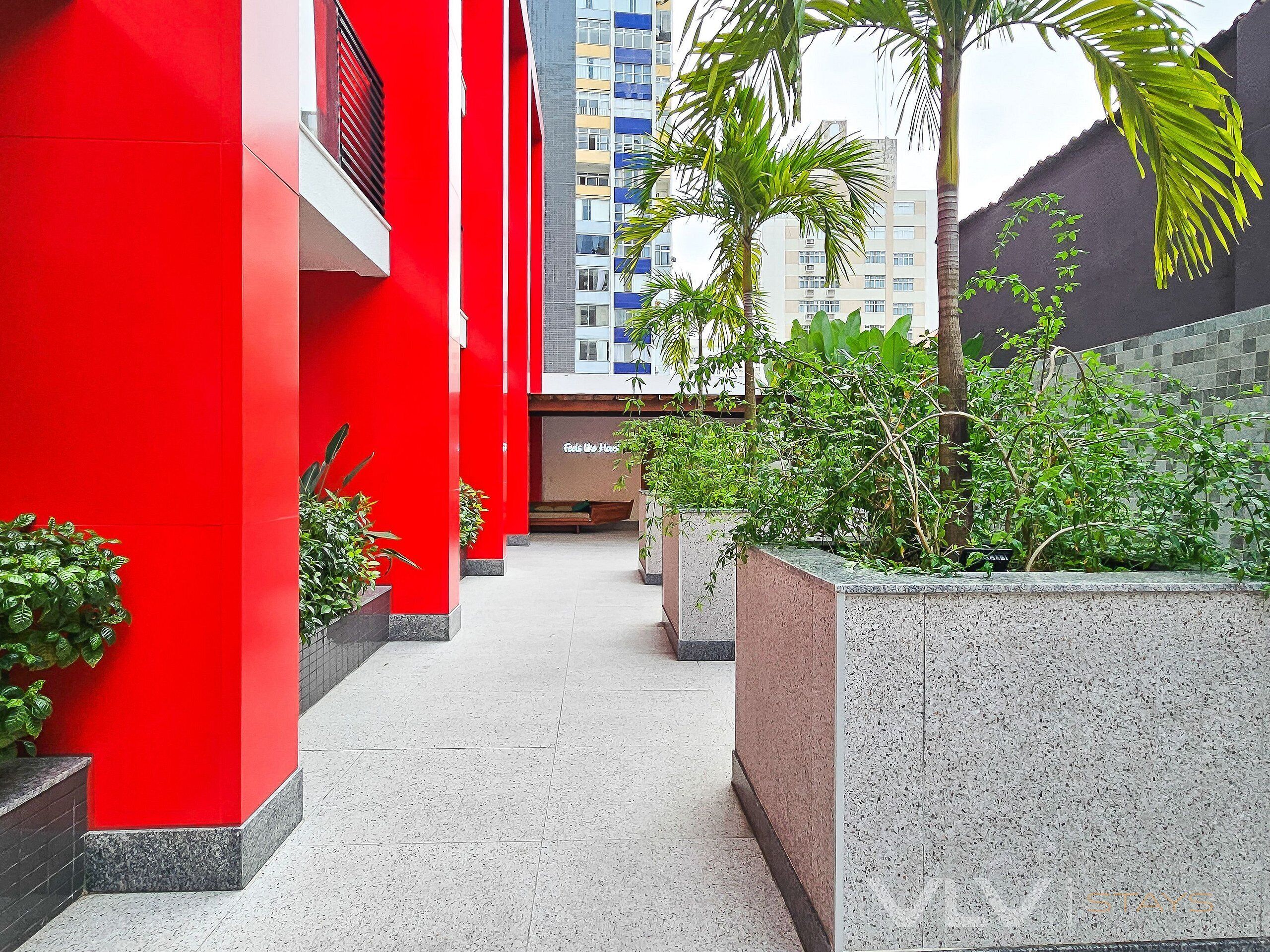 Un pasillo con paredes rojas, plantas en macetas y una vista de un edificio de gran altura al fondo.
