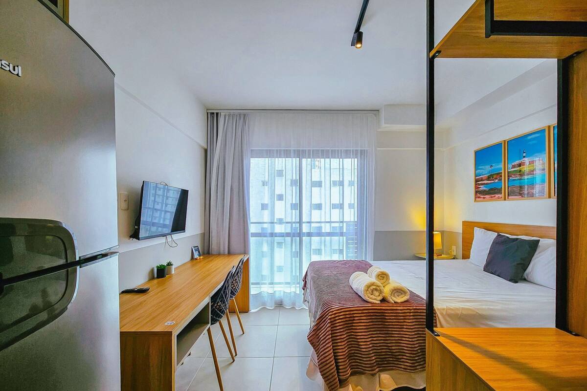 Una habitació d'hotel amb llit, escriptori amb cadira, televisió i finestra amb cortines.