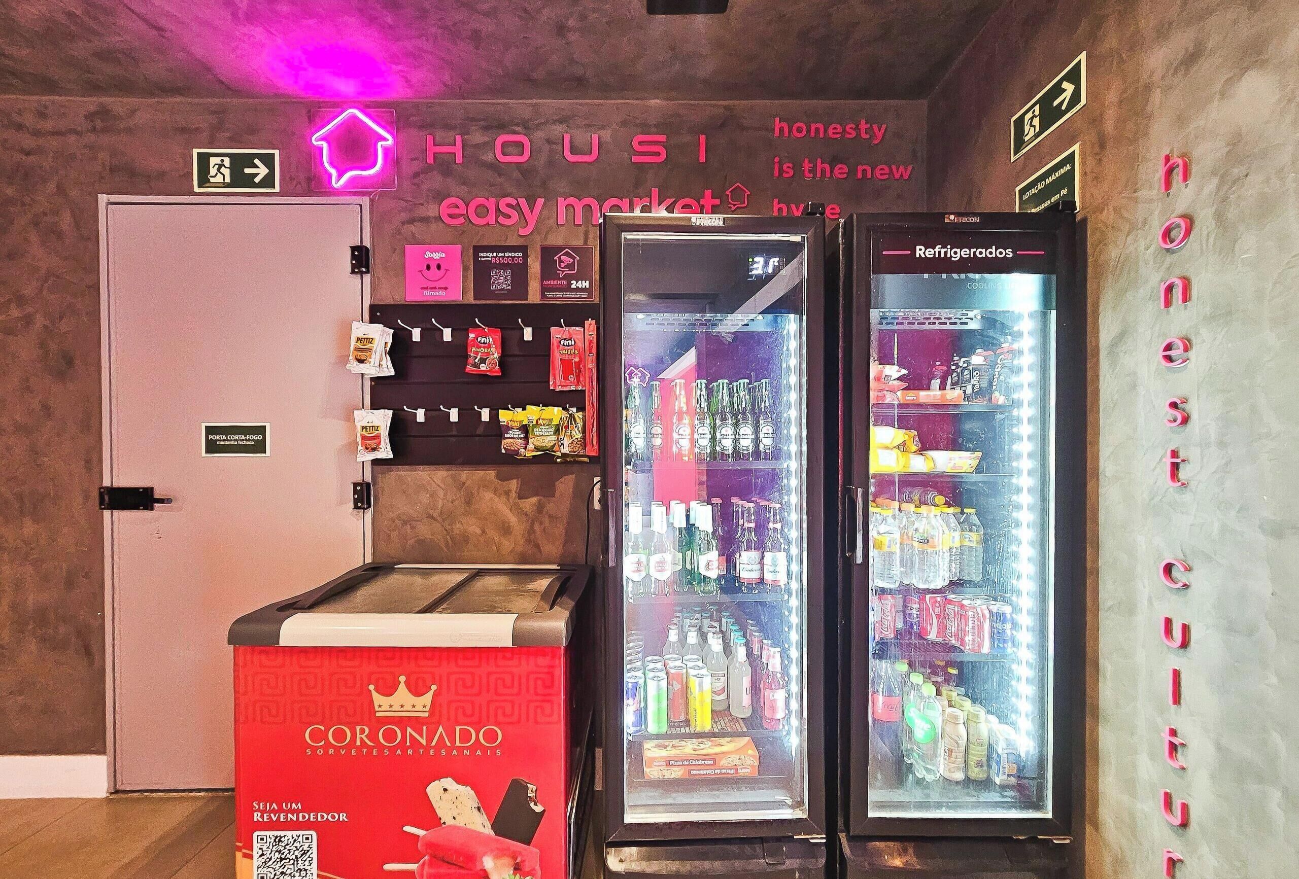 Un vestíbulo de hotel con un letrero de neón, un refrigerador y un mostrador rojo con un código QR.