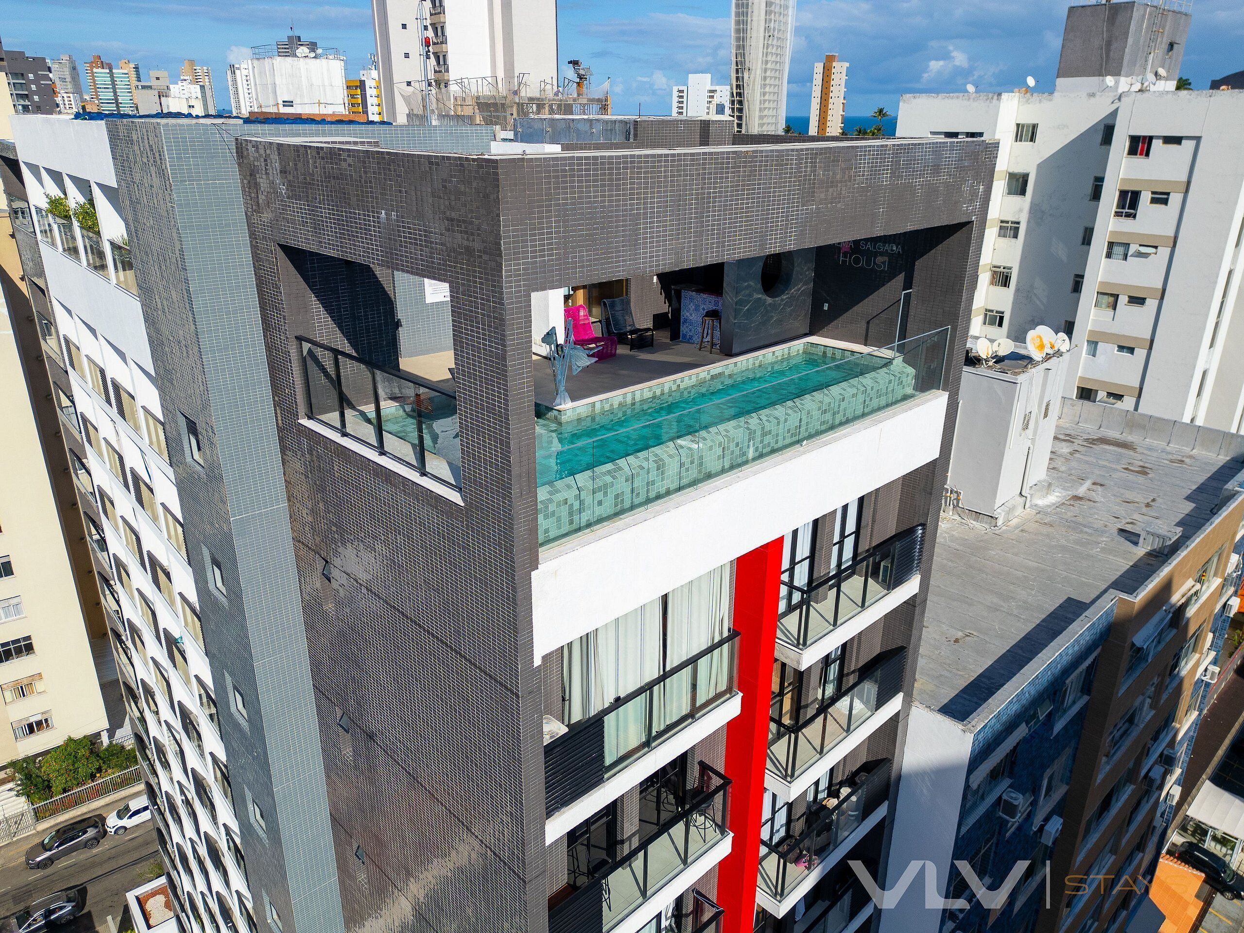 A modern building with a rooftop pool, balconies, and a red vertical feature.