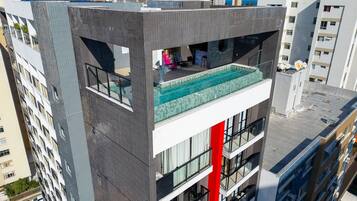 A modern building with a rooftop pool, balconies, and a red vertical feature.