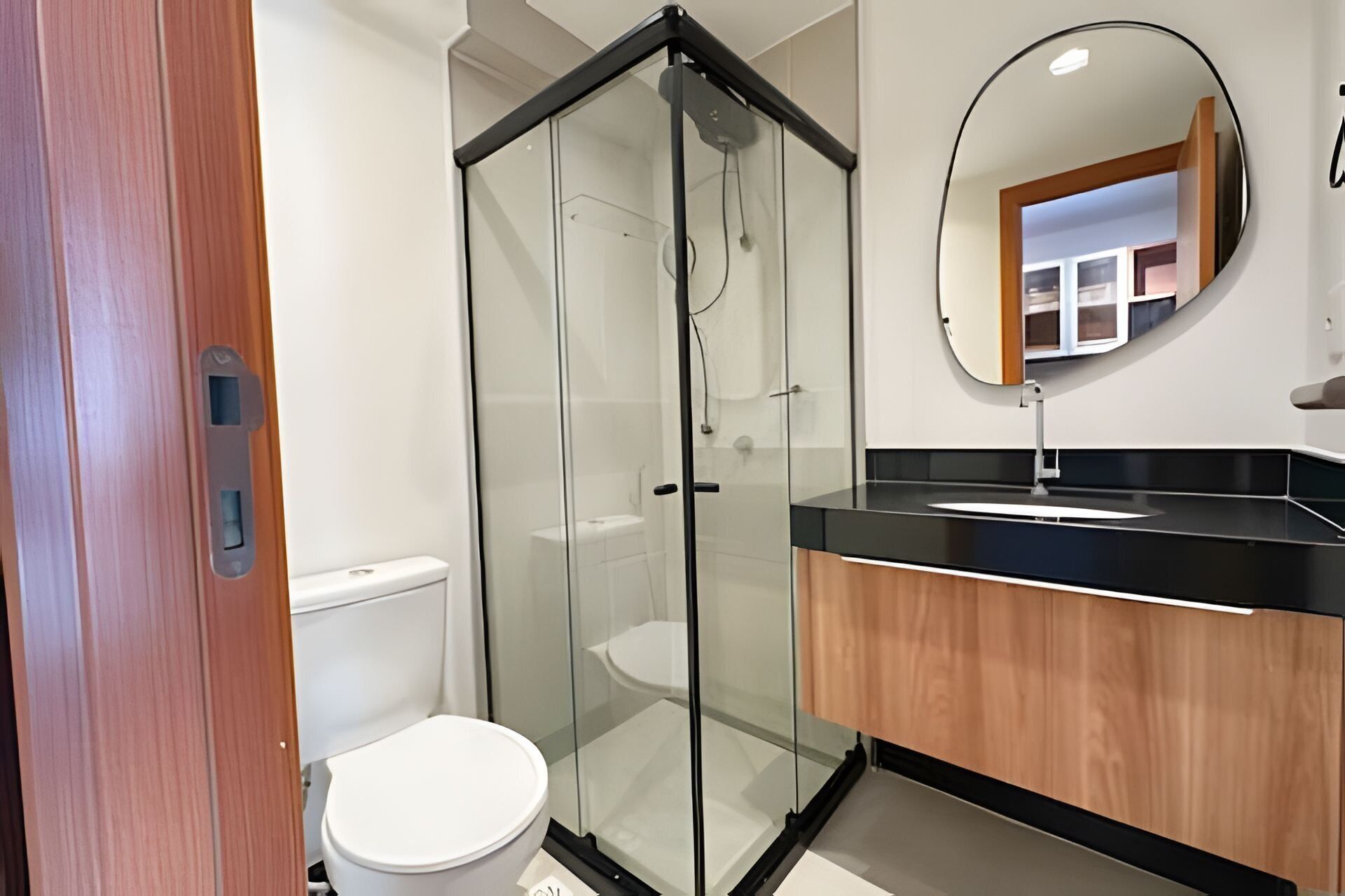 Een moderne badkamer met een douchecabine van glas, een wit toilet en een zwart wastafelmeubel met houten details.