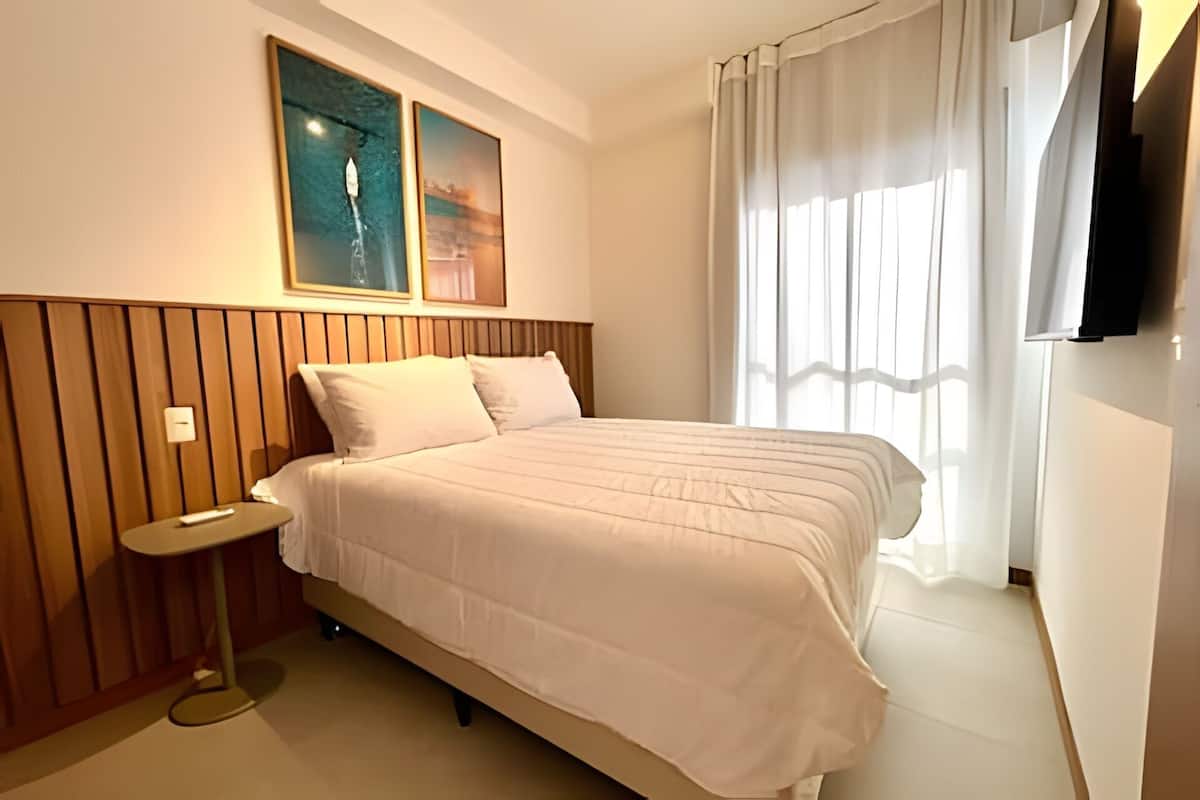 Habitació d'hotel amb llit, una taula de nit, televisió penjada a la paret i finestra amb cortines.