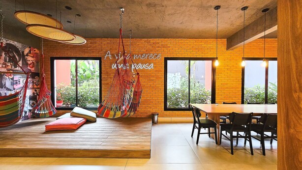 A modern interior with a brick wall, large windows, a hanging hammock, and a dining area. - Porto Privilege by VLV Stays (Salvador)