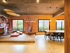 A modern interior with a brick wall, large windows, a hanging hammock, and a dining area.