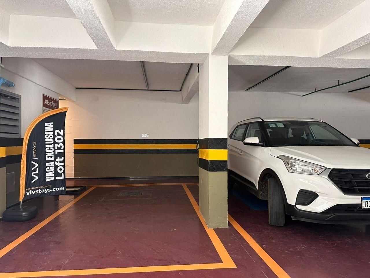 A parking garage with a white car parked in a spot marked 'VAGA EXCLUSIVA Loft 1302'.
