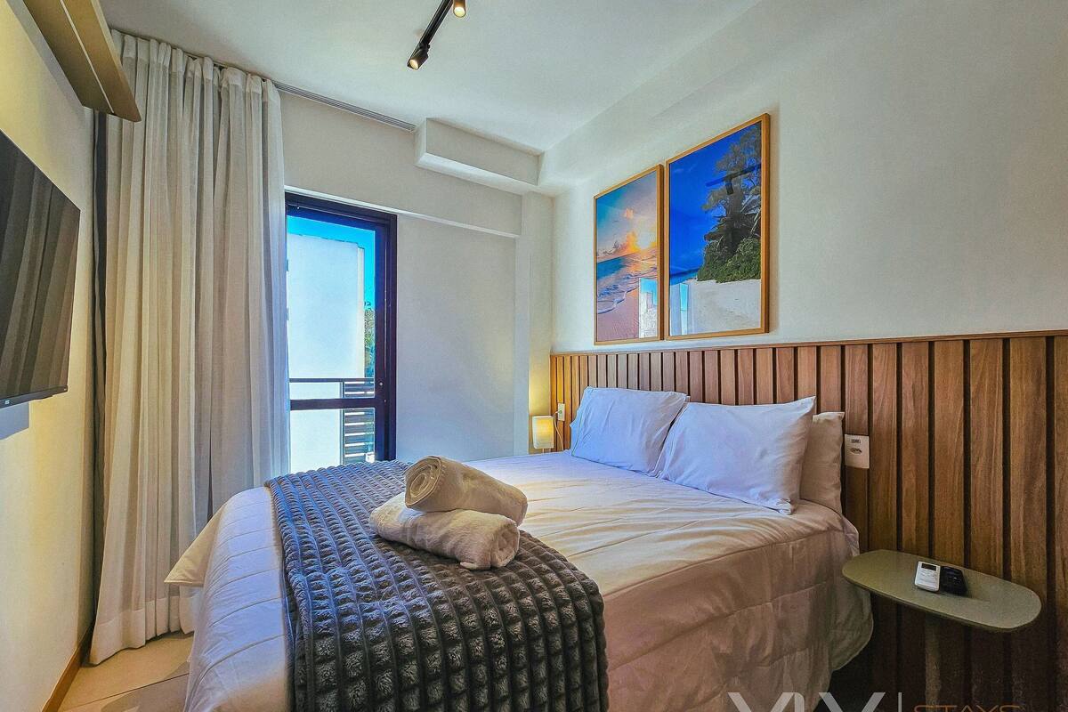 Una habitació d'hotel amb un llit, una taula de nit, una finestra amb cortines i un quadre a la paret.