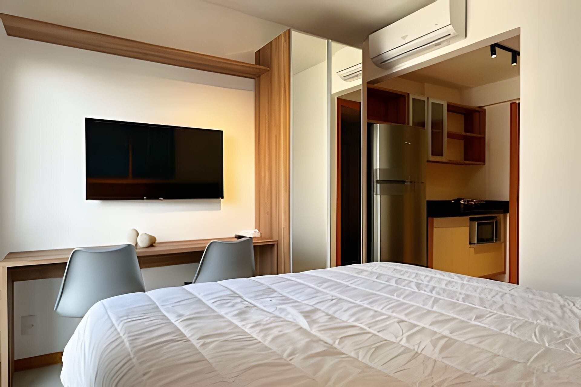 Habitación de hotel con cama, escritorio con dos sillas, televisor, refrigerador y kitchenette.