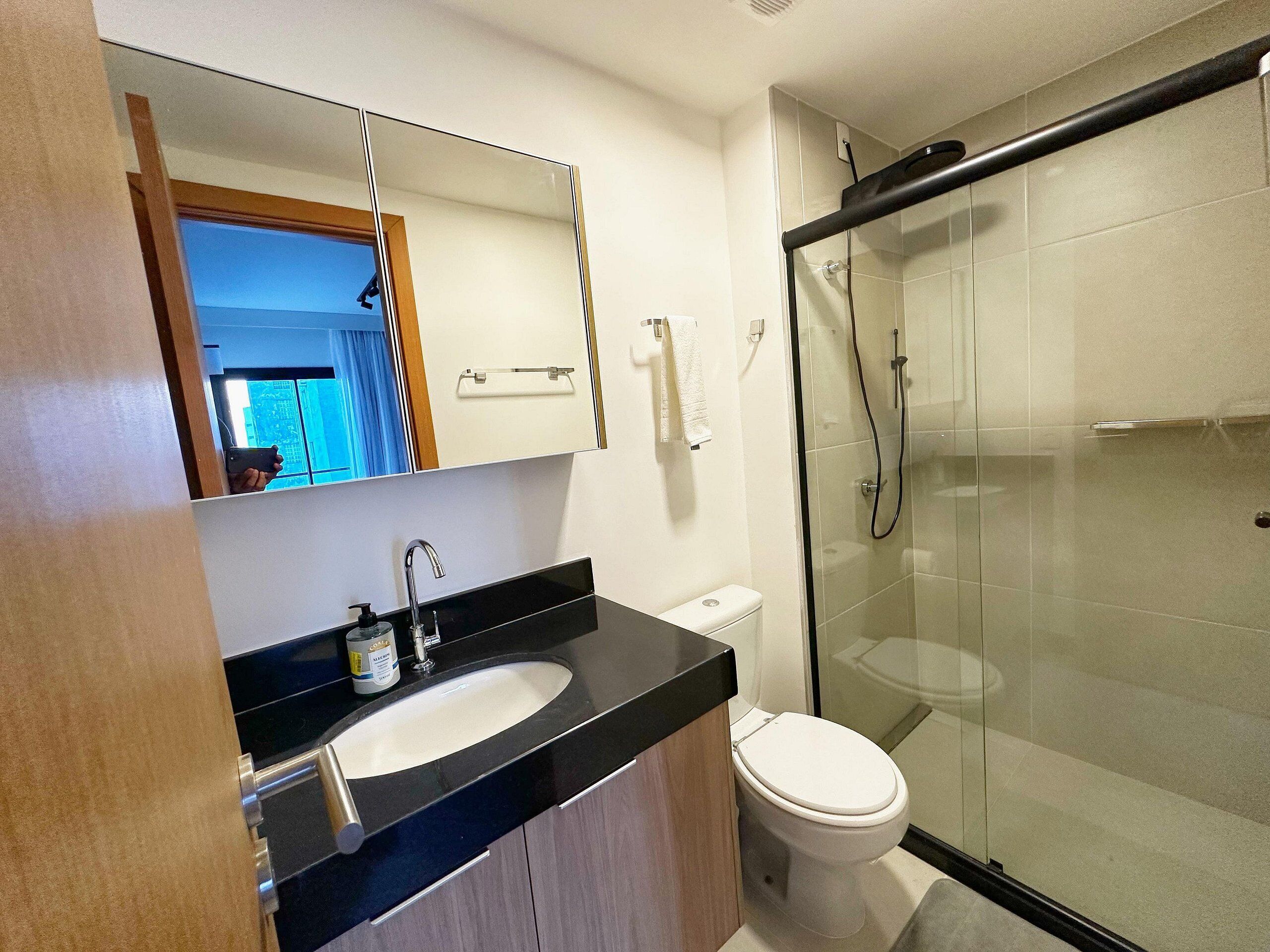 A modern bathroom with a glass shower enclosure, a white toilet, and a black countertop with a sink.