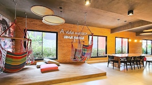 A modern interior with a brick wall, large windows, a hammock chair, and a wooden table. - Porto Privilege by VLV Stays (Salvador)