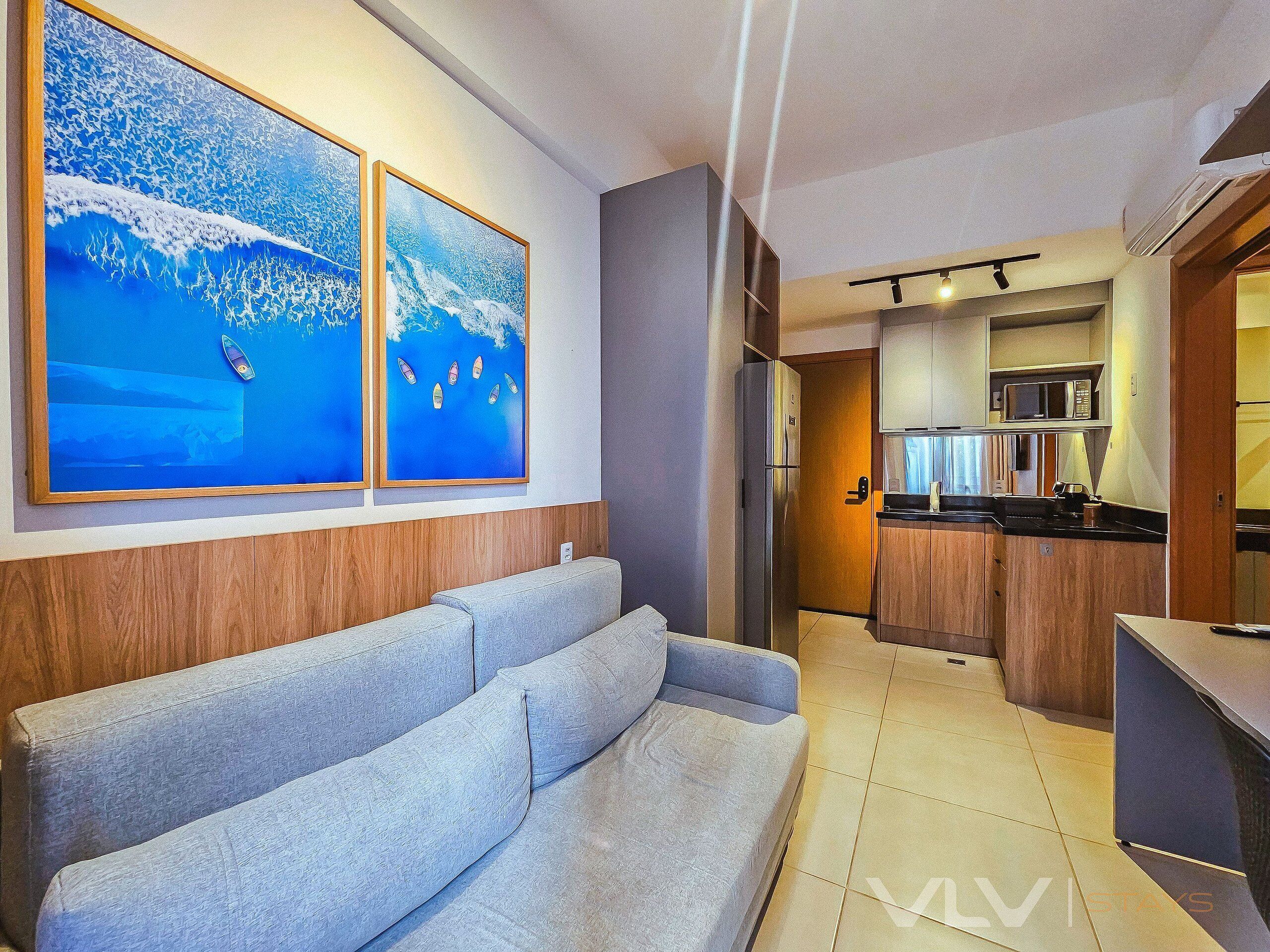 A modern living area with a sofa, a kitchen with a microwave, and two framed artworks on the wall.