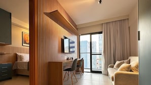 A modern living room with a sofa, a TV, a desk with a chair, and a large window. - Porto Privilege by VLV Stays (Salvador)