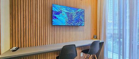 A modern room with a wooden panel wall, a flat-screen TV, a desk, two chairs, and a window with curtains.