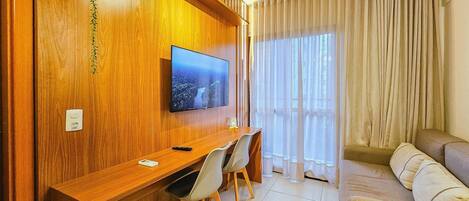 Una sala de estar moderna con un escritorio de madera, un televisor de pantalla plana, un sofá y un ventanal con cortinas.