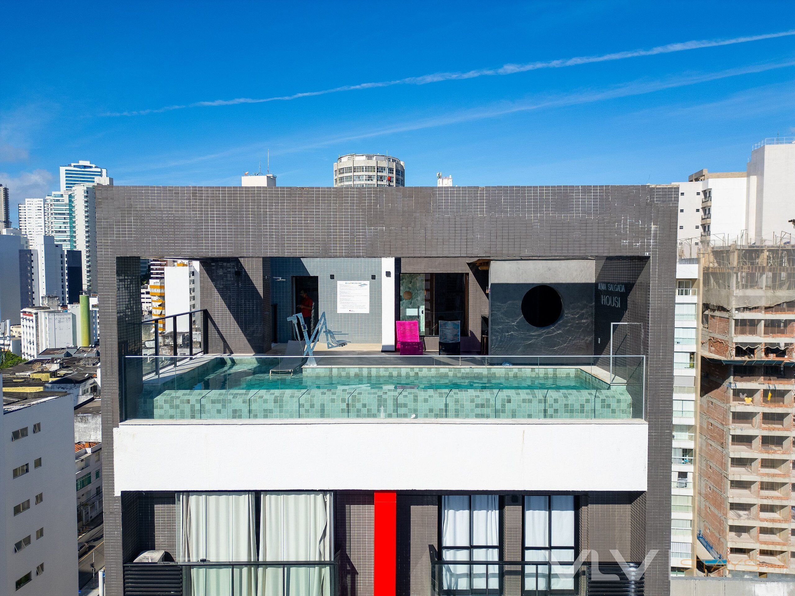 En moderne bygning med pool på taget, stort vindue og skilt med 'KUMASALGA HOUSE'.