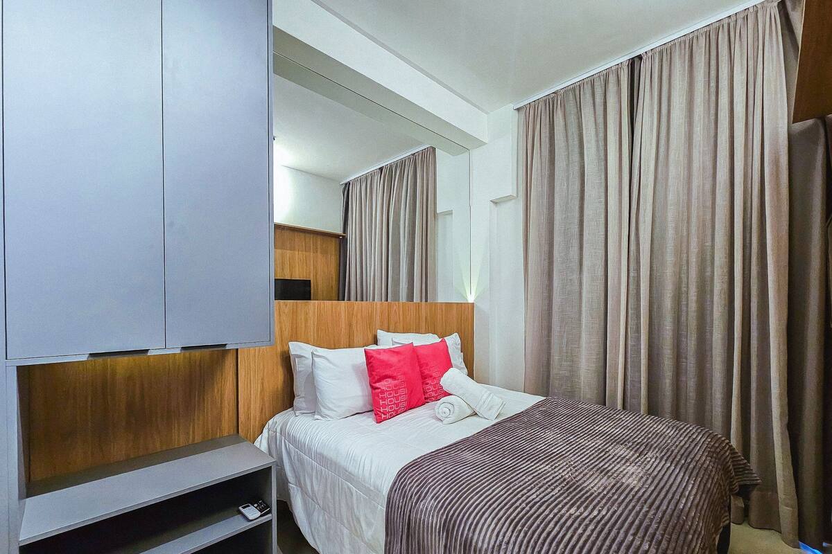 Habitació d'hotel amb un llit, una televisió, un panell de capçalera de fusta i cortines.