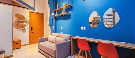 Un interior moderno con una pared azul de acento, un sofá, dos sillas rojas, un escritorio de madera y un espejo.