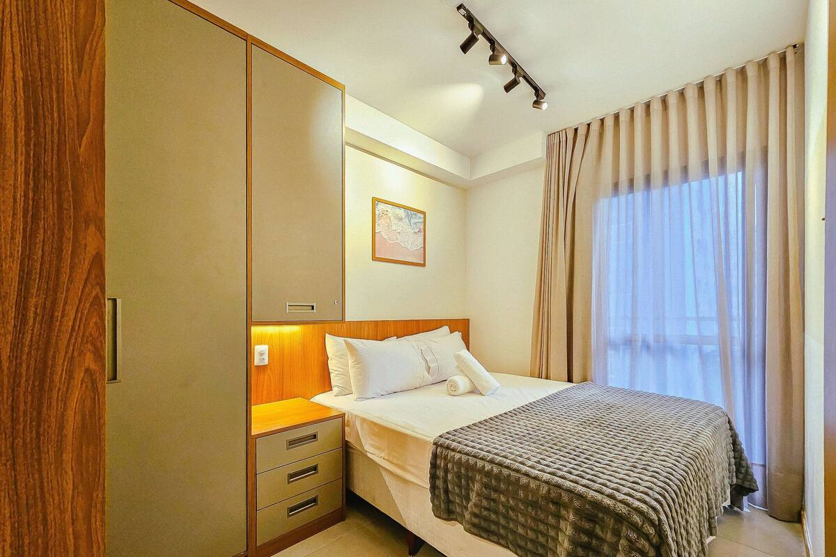 Habitació d'hotel amb llit, armari, taula de nit i finestra amb cortines.