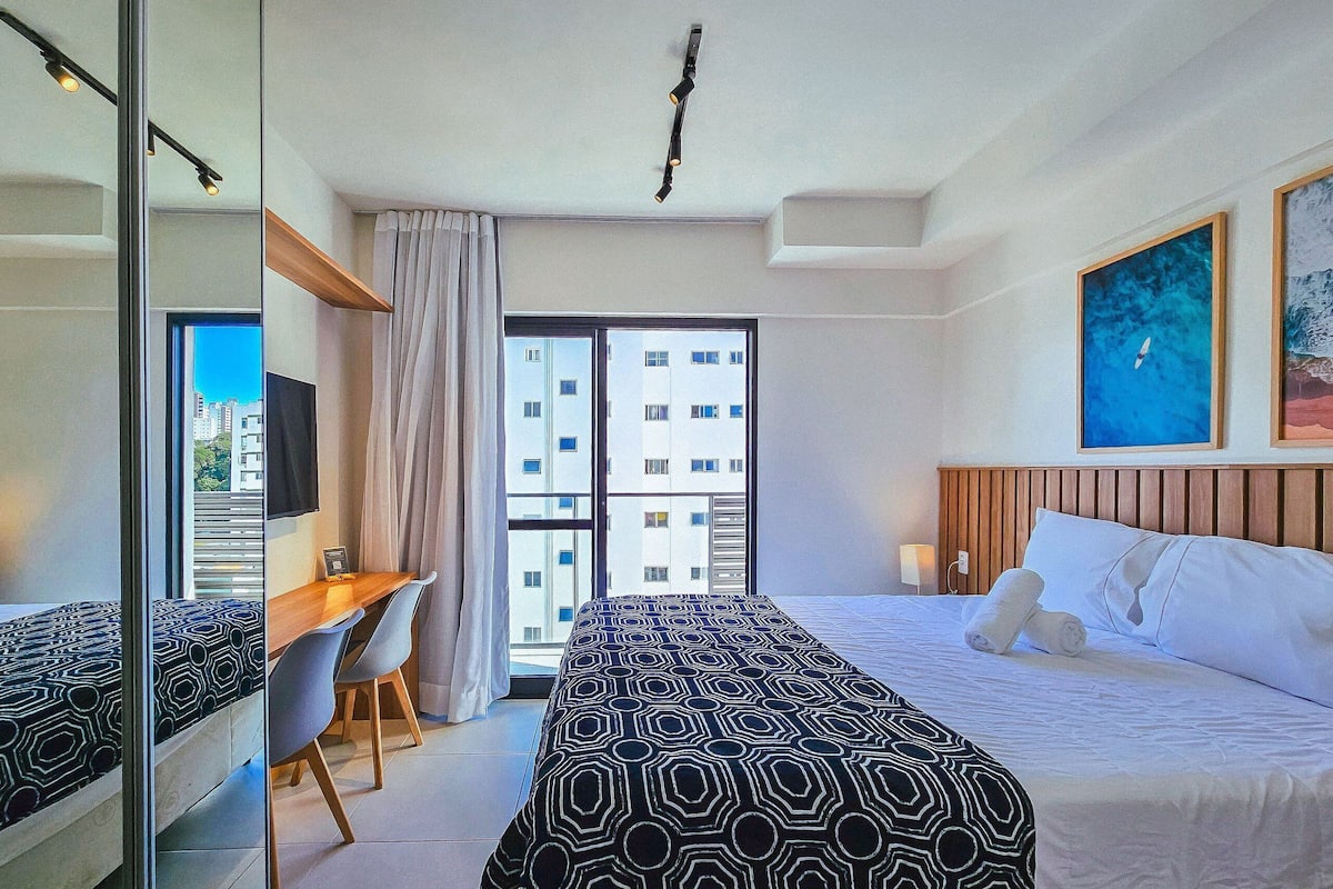 Habitació d'hotel amb llit, escriptori, cadira, televisió i finestra gran.
