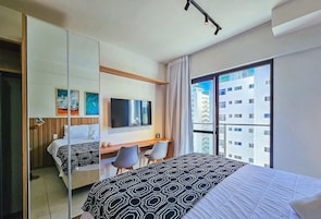 A hotel room with a bed, a desk, a chair, a TV, and a large window with a city view.