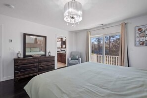A bedroom with a large bed, a dresser, a chair, a chandelier, and a view through a window.