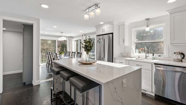 A modern kitchen with a marble island, stainless steel appliances, and a dining area with bar stools. - Sakura House: Spacious 4BR w/ Gym & Premium Design (Northborough)