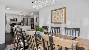 A dining area with a wooden table and chairs, a chandelier, and a framed picture on the wall. - Sakura House: Spacious 4BR w/ Gym & Premium Design (Northborough)
