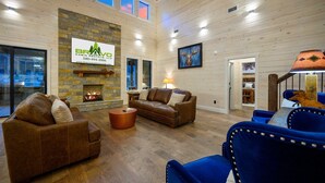 A cabin interior with a stone fireplace, wooden walls, and a blue sofa. - Rare Breed | 8 Bedrooms | Pool | Pickleball | Playset | ATV access (Broken Bow)
