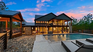 A modern two-story house with a swimming pool, outdoor seating, and a covered patio area. - Rare Breed | 8 Bedrooms | Pool | Pickleball | Playset | ATV access (Broken Bow)