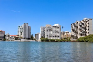 A waterfront cityscape with modern high-rise buildings, a clear blue sky, and calm water. - Condado Steps From the Beach Nightlife (San Juan)