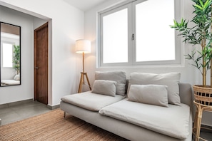 A modern living room with a sofa, a lamp, a mirror, and a large window. - Condado Steps From the Beach Nightlife (San Juan)