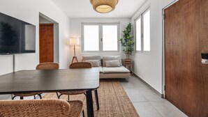 Una sala moderna con una mesa de comedor de madera oscura, sillas de mimbre, un sofá y un ventanal grande.