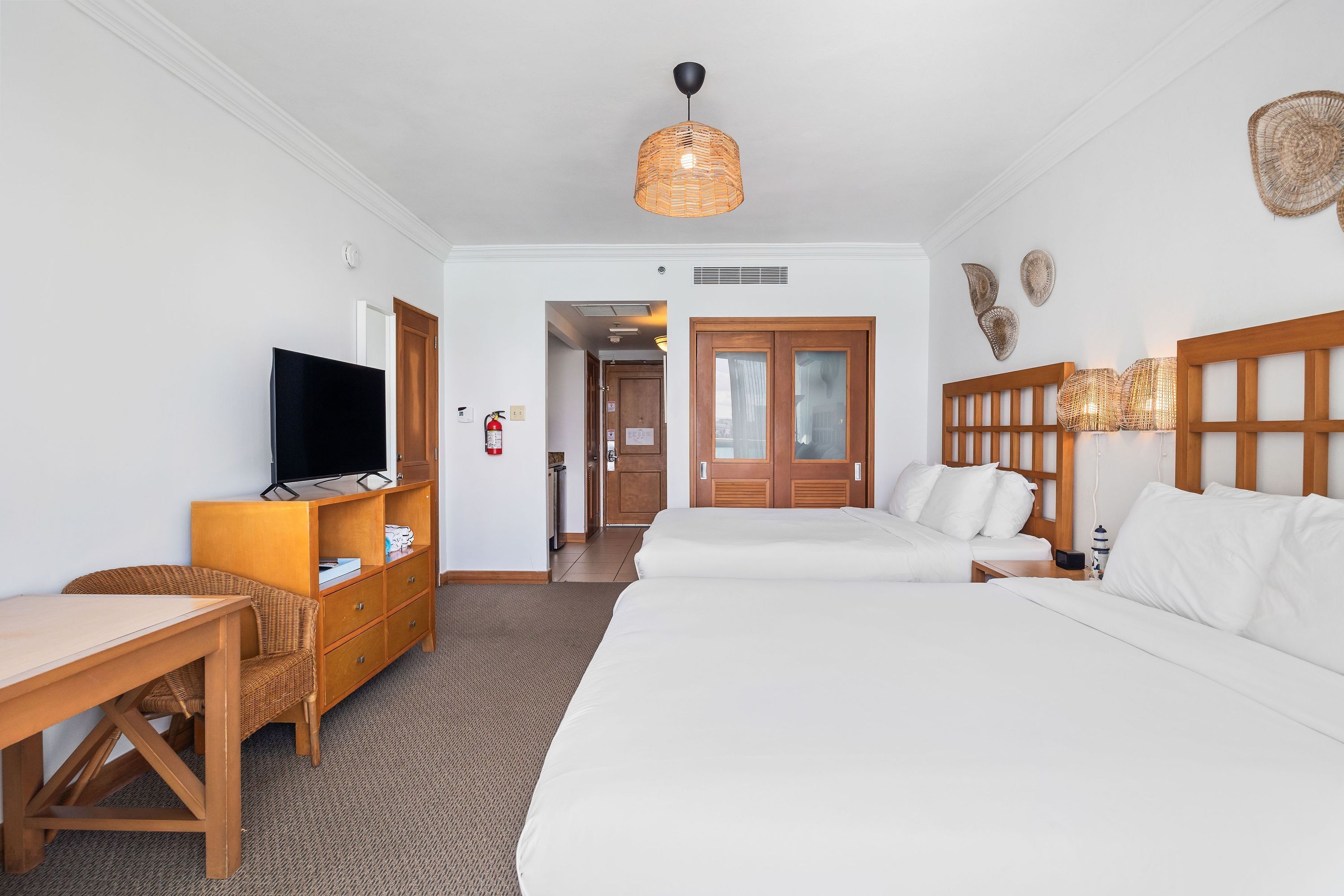 A hotel room with a bed, a desk, a television, and a wicker chair.