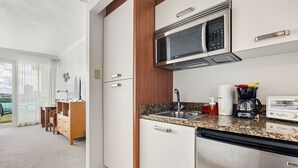 A modern kitchen with a stainless steel refrigerator, microwave, and sink. There is a dining area with a table and chairs visible through a glass door. - Condado Beach View Balcony Condado Beach (San Juan)