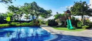 A swimming pool surrounded by lush greenery and a slide. - City Skyline View at Air Residences (Makati)