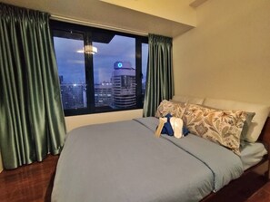Ein Hotelzimmer mit einem großen Bett, grünen Vorhängen und Blick auf eine Stadtlandschaft im Abenddämmerung.