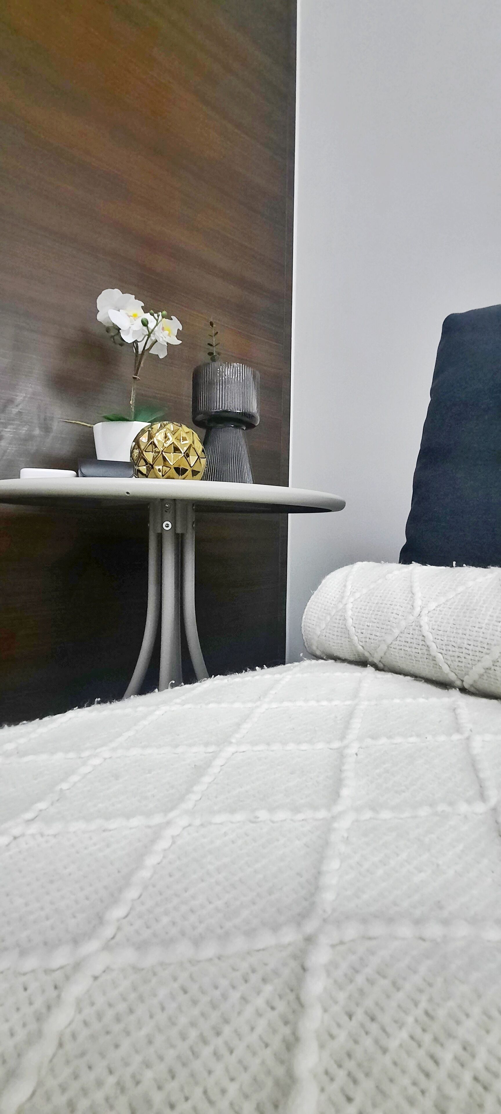 A neatly arranged bedroom with a bed, a small table with a potted plant, and a decorative vase.